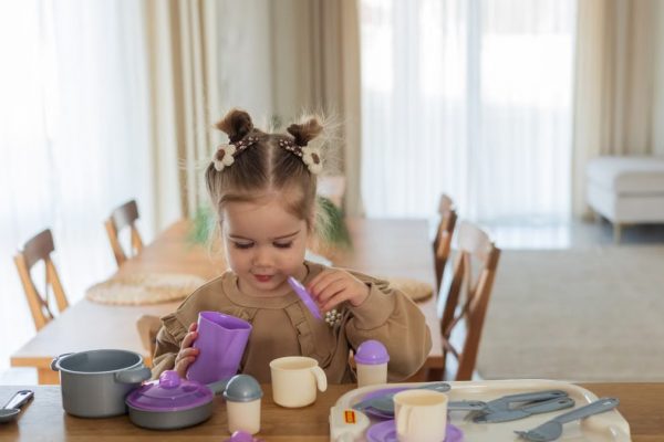 A young girl playing with a colorful toy tea set on a wooden table indoors.