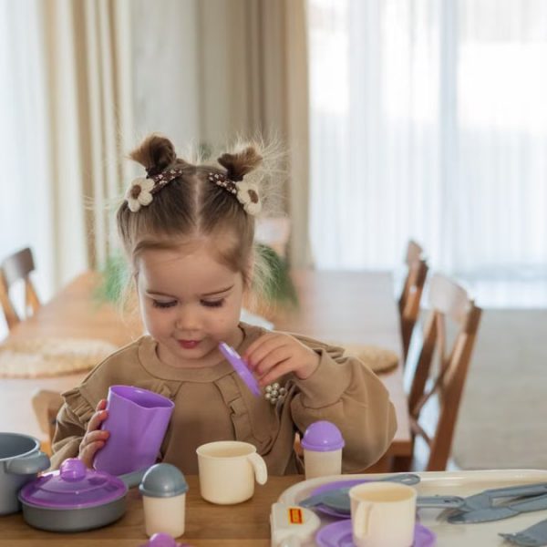 A young girl playing with a colorful toy tea set on a wooden table indoors.