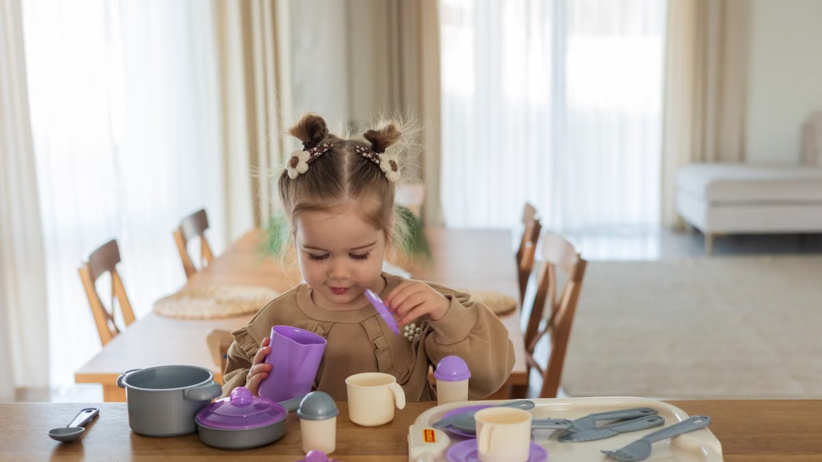 A young girl playing with a colorful toy tea set on a wooden table indoors.